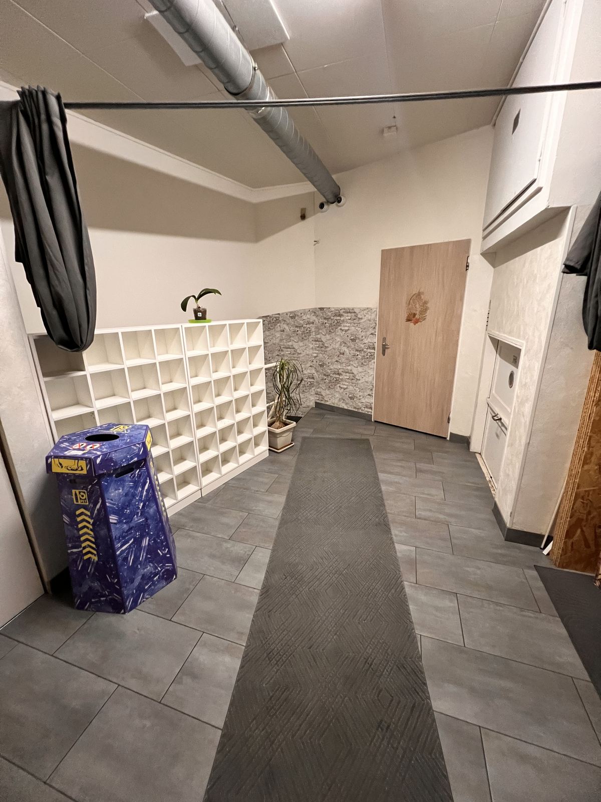 Geflister Vorraum mit weissen Schuhfächern an der Wand, einem grauen Läufer und einer Holztür.