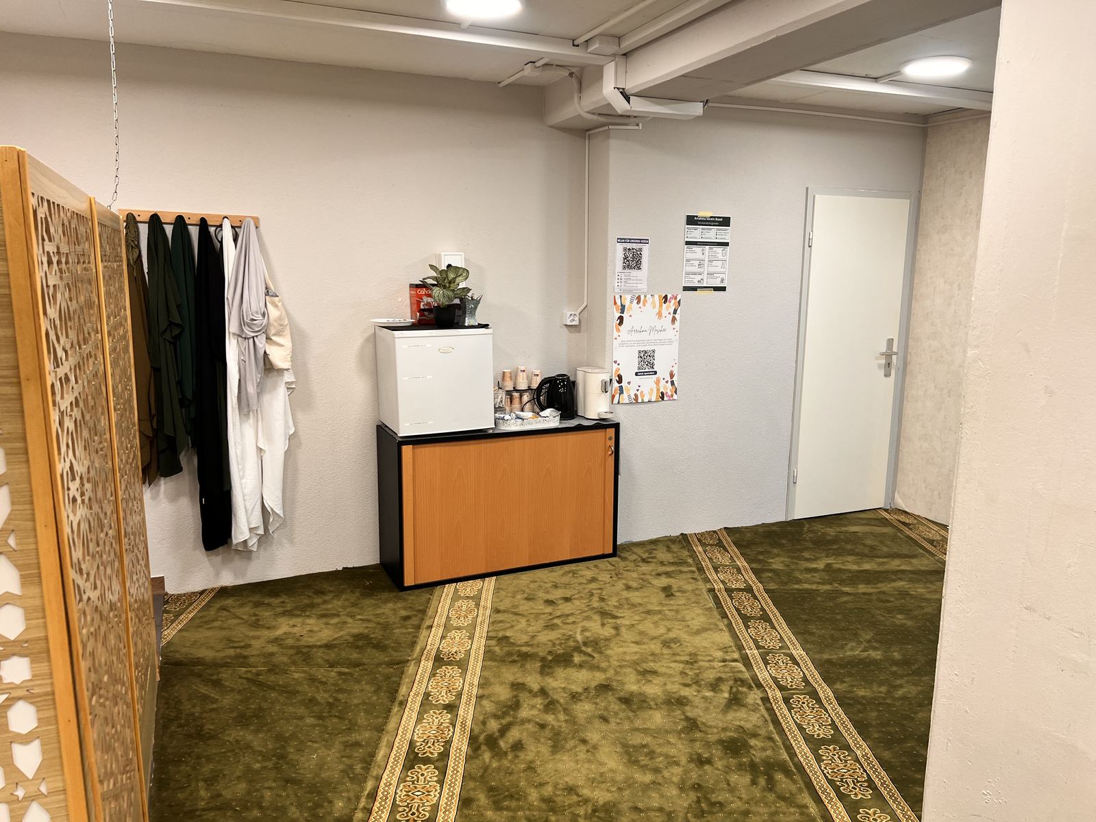Ecke im Frauenraum mit Kleiderstange, einem kleinen Tresen mit Wasserkocher und einer Ornamentwand.